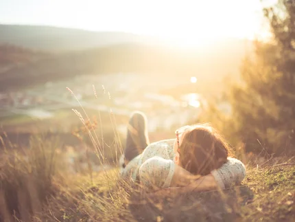 Frau liegt im Gras mit Blick auf sonnige Landschaft und Hügel