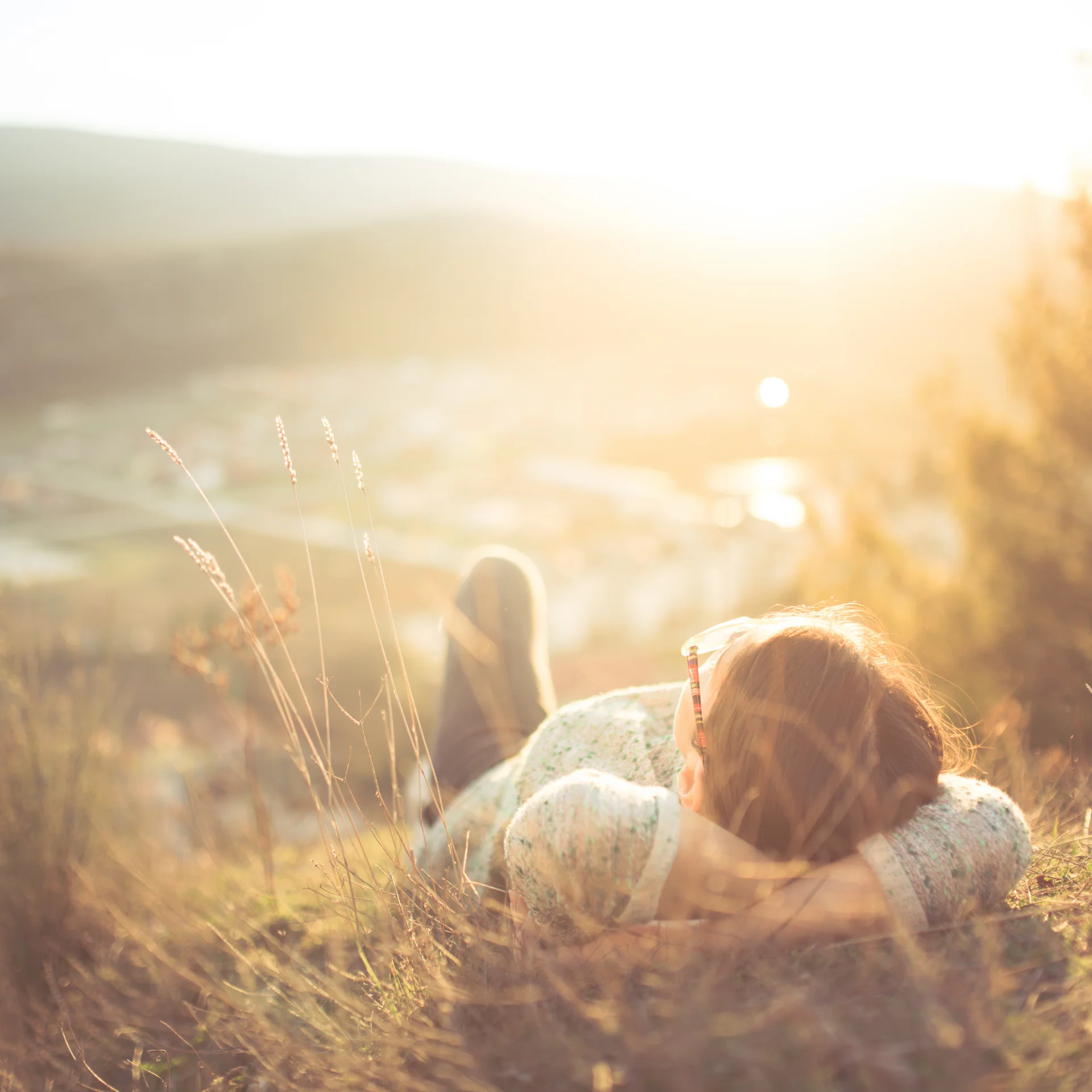 Frau liegt im Gras mit Blick auf sonnige Landschaft und Hügel