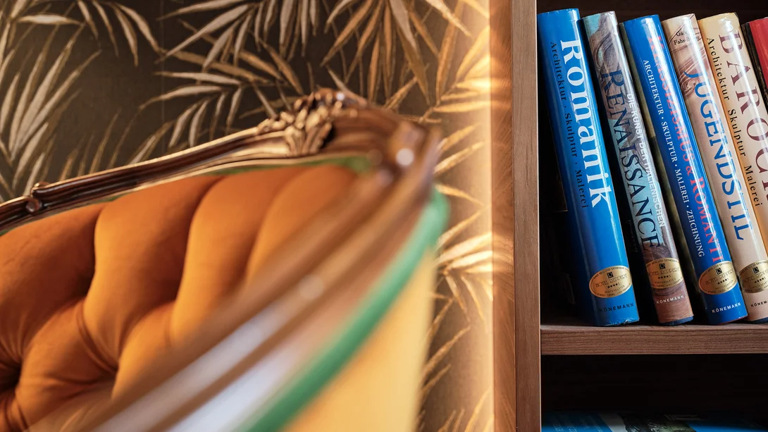 Nahaufnahme eines Bücherregals mit Architektur- und Kunstbüchern neben einem orangefarbenen Sessel