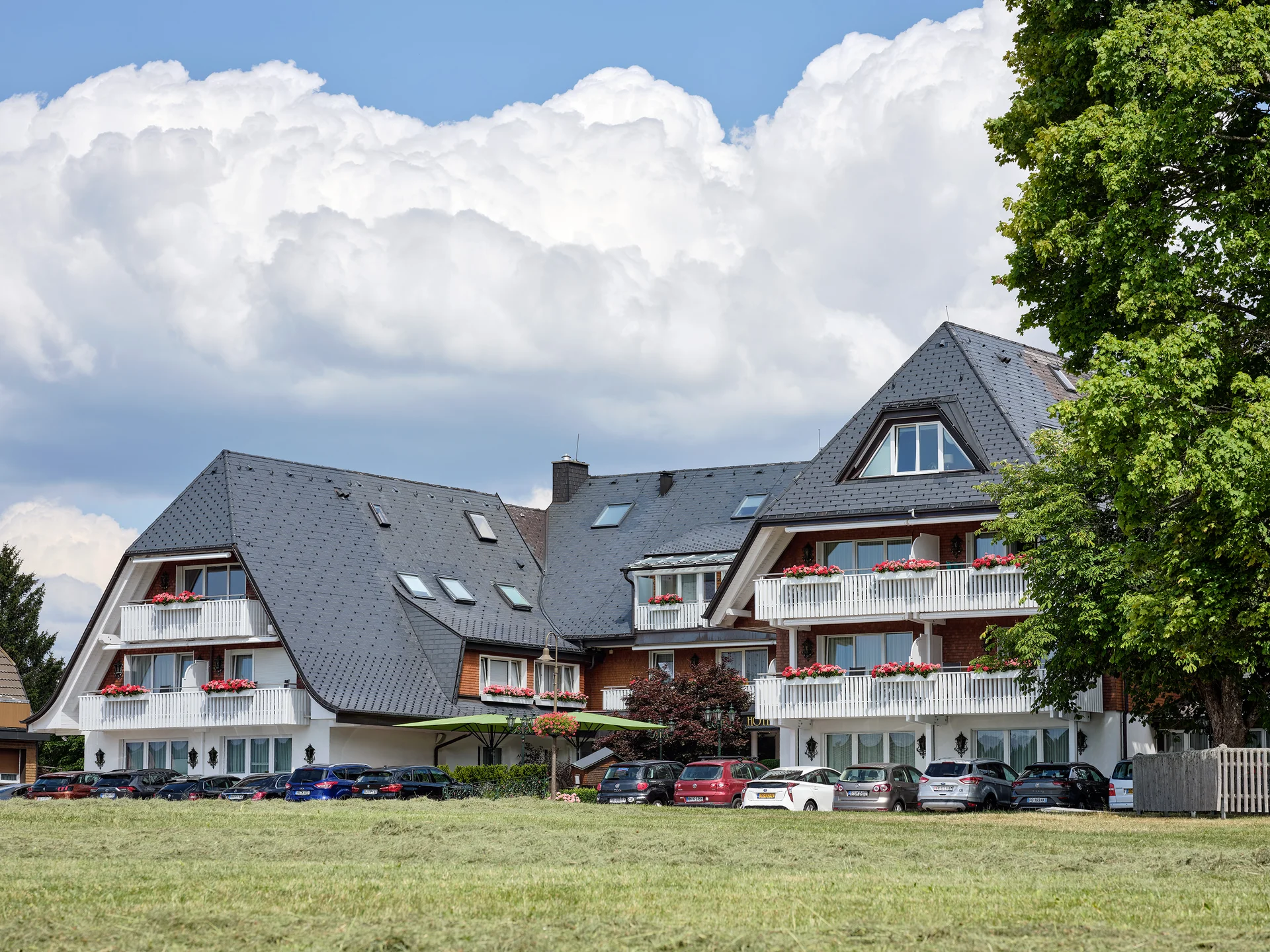 Hotelgebäude mit grauem Schrägdach und Balkonen mit roten Blumen