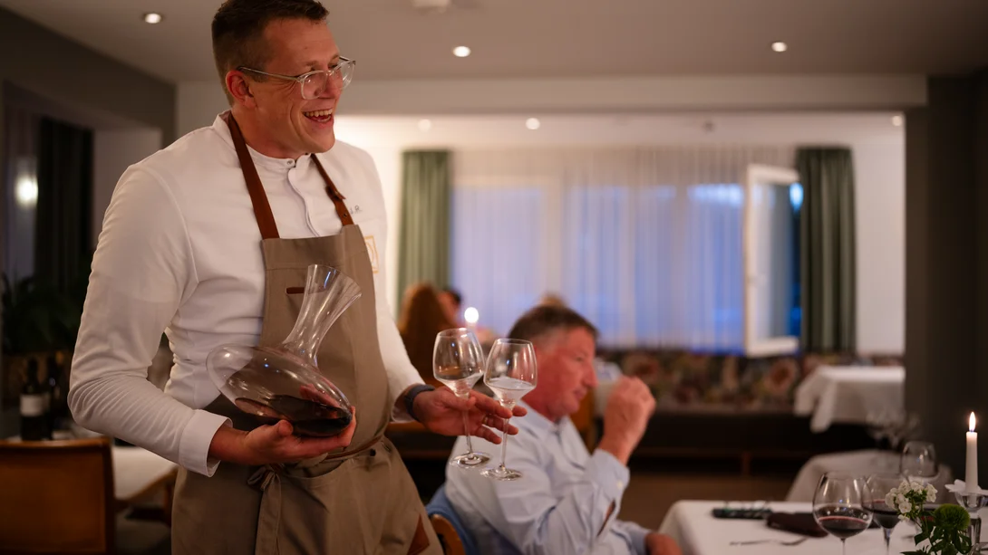 Fröhlicher Kellner mit Dekanter und Weingläsern im Restaurant