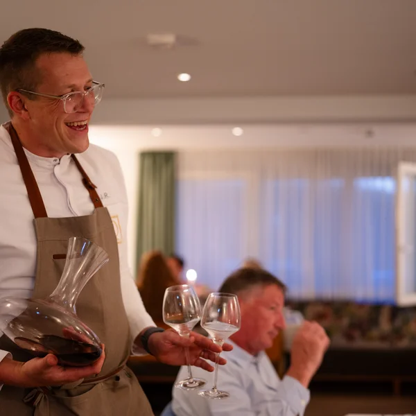 Fröhlicher Kellner mit Dekanter und Weingläsern im Restaurant