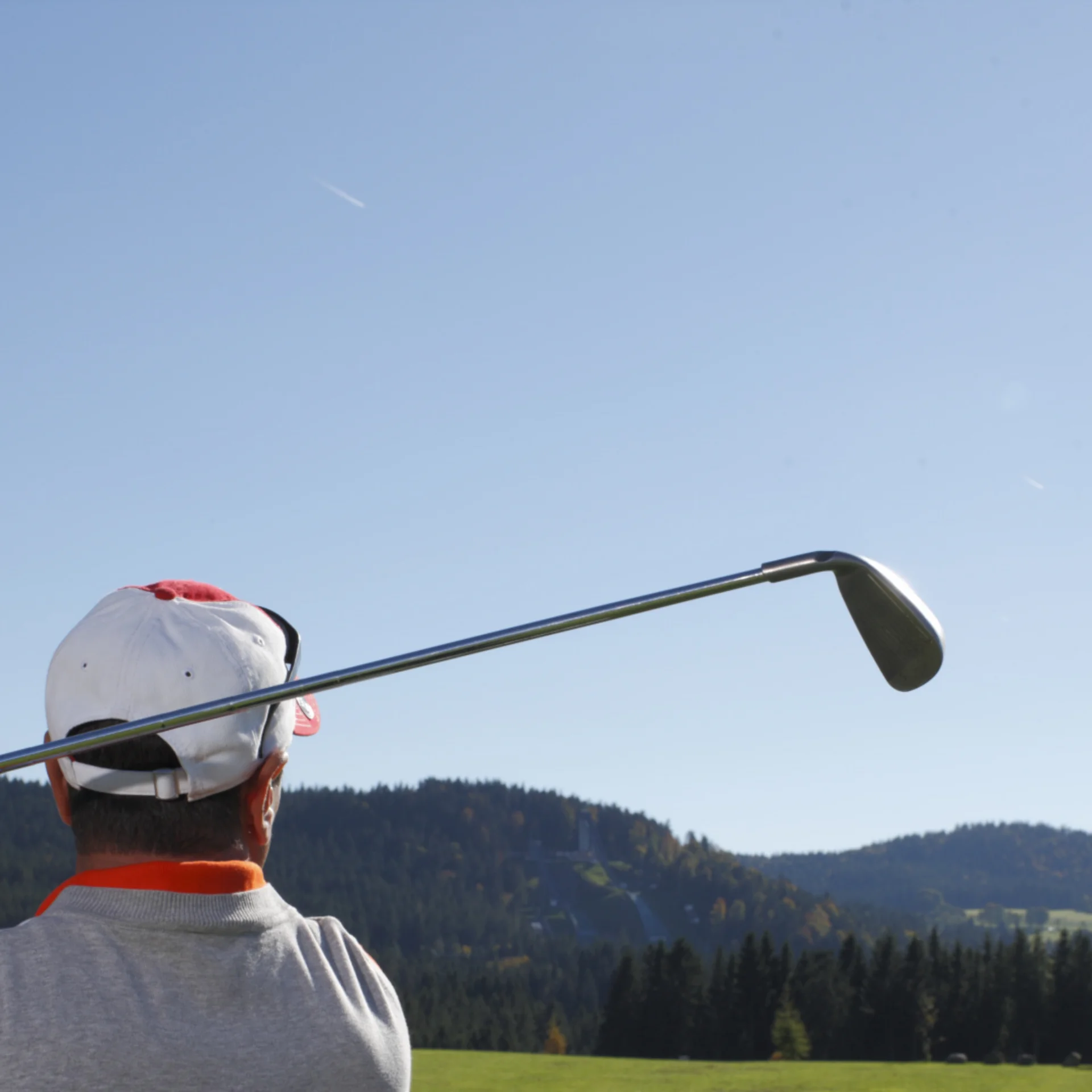 Golfspieler von hinten beim Abschlag auf einem grünen Golfplatz mit Bergen