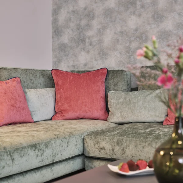Ecksofa mit roten Kissen und unscharfer Vase mit Blumen im Vordergrund