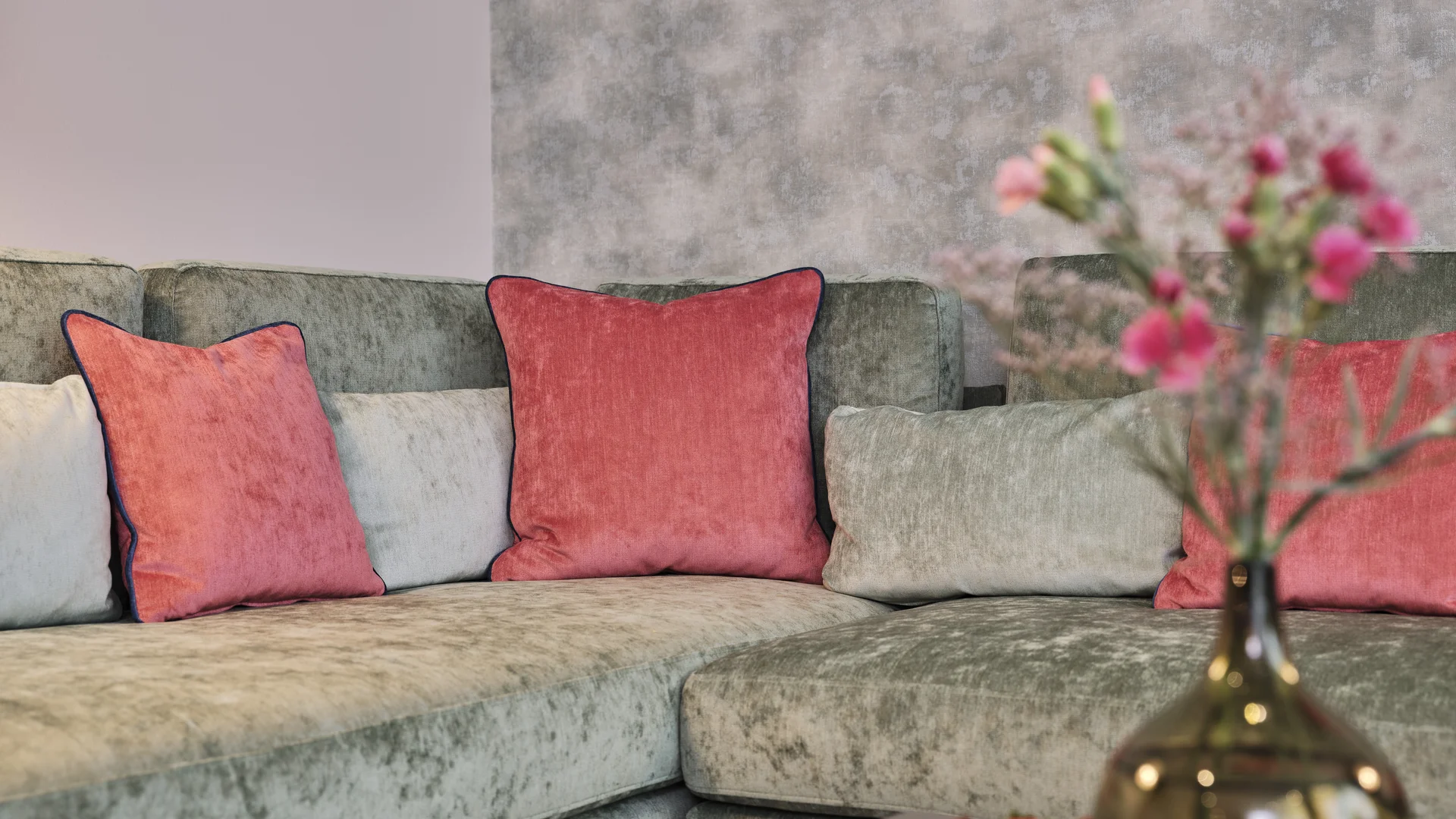 Ecksofa mit roten Kissen und unscharfer Vase mit Blumen im Vordergrund