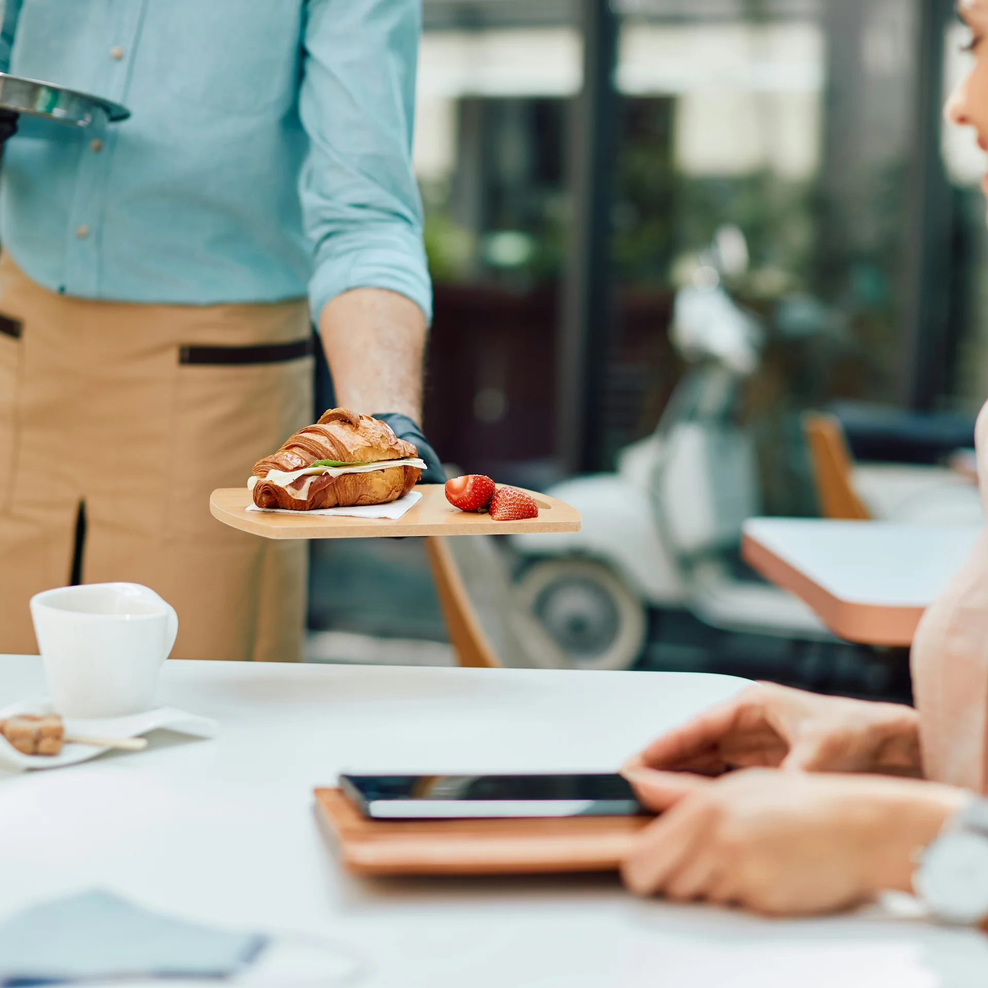 Kellner serviert Croissant mit Erdbeeren an Gast im Café