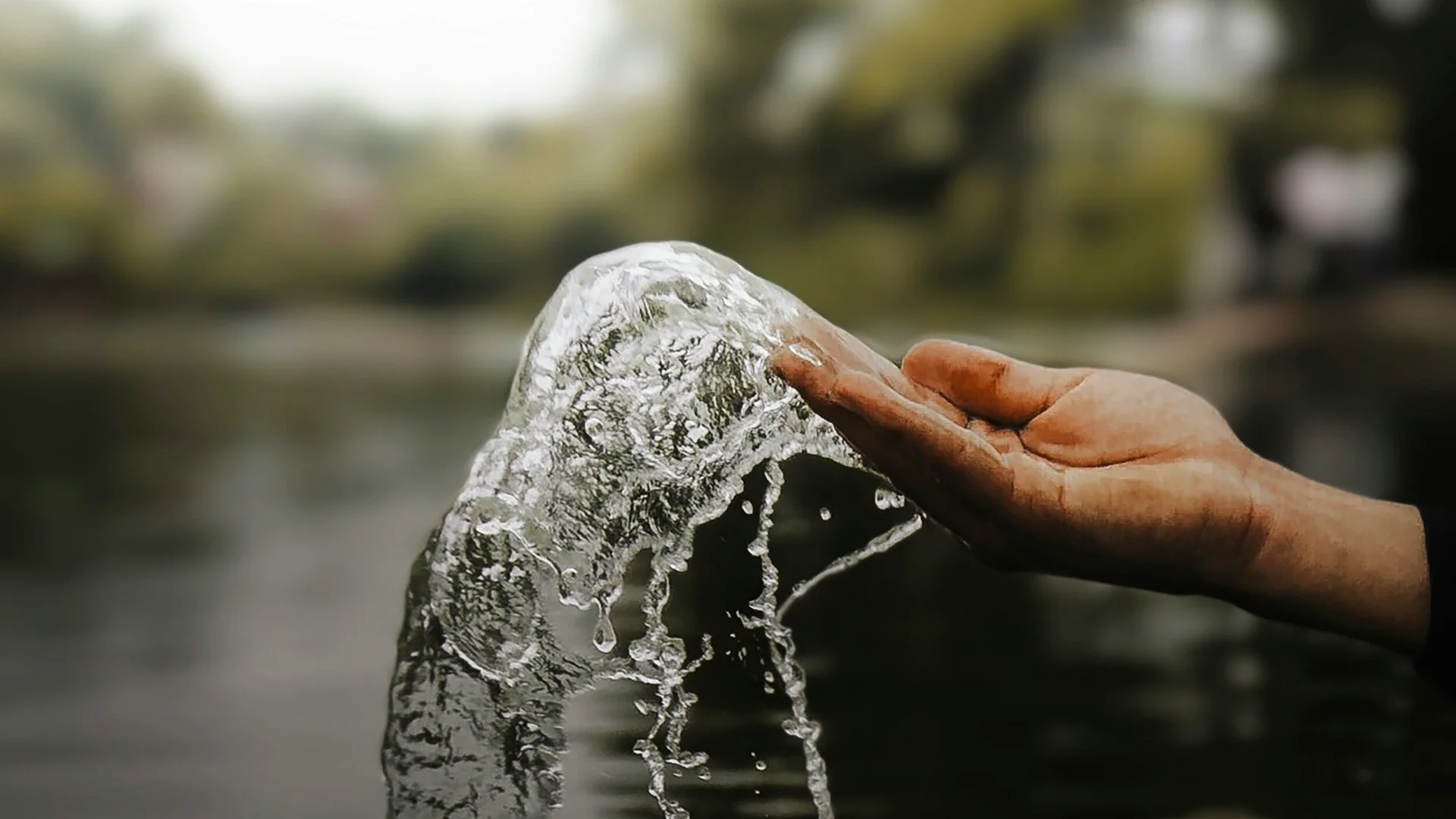 Hand fängt spritzendes Wasser über dem Fluss mit verschwommenem Hintergrund