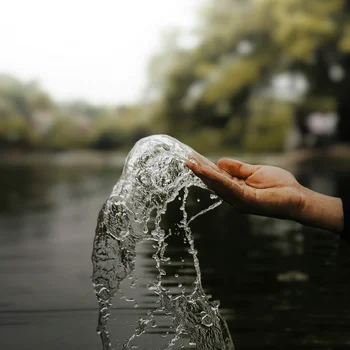 Hand fängt spritzendes Wasser über dem Fluss mit verschwommenem Hintergrund