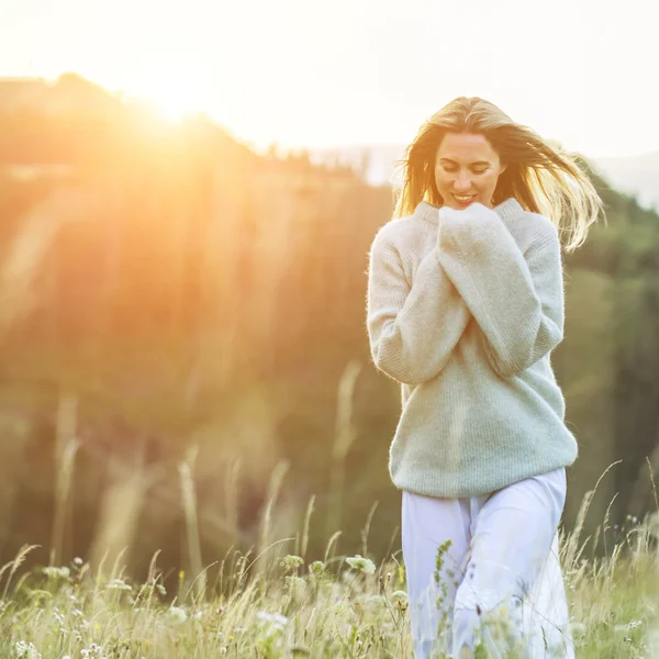 Frau im Pullover in einem sonnigen Blumenwiese, Berge im Hintergrund