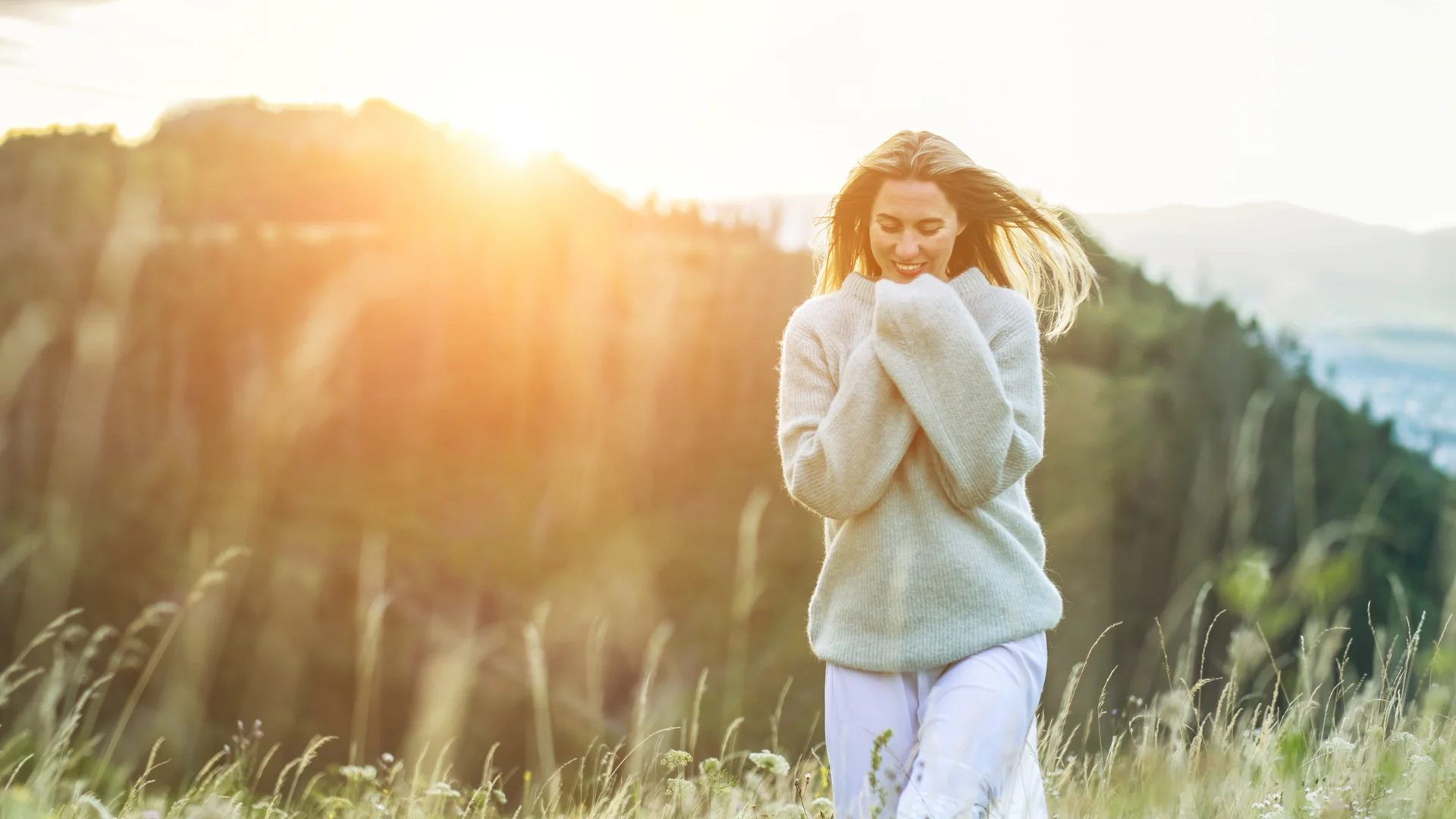 Frau im Pullover in einem sonnigen Blumenwiese, Berge im Hintergrund