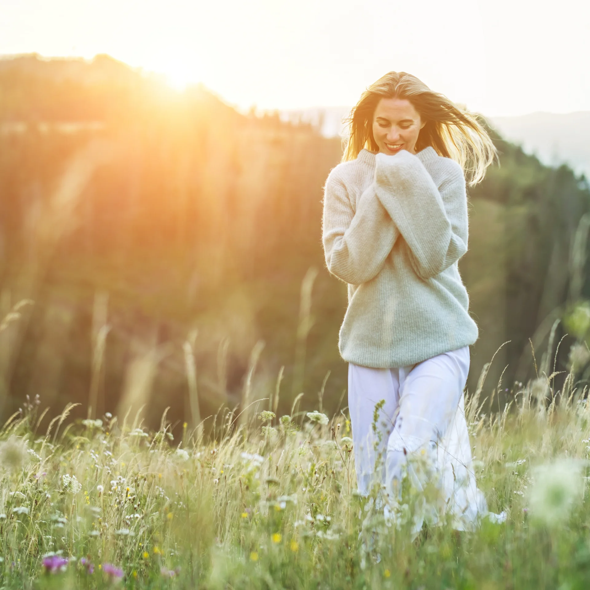 Frau im Pullover in einem sonnigen Blumenwiese, Berge im Hintergrund