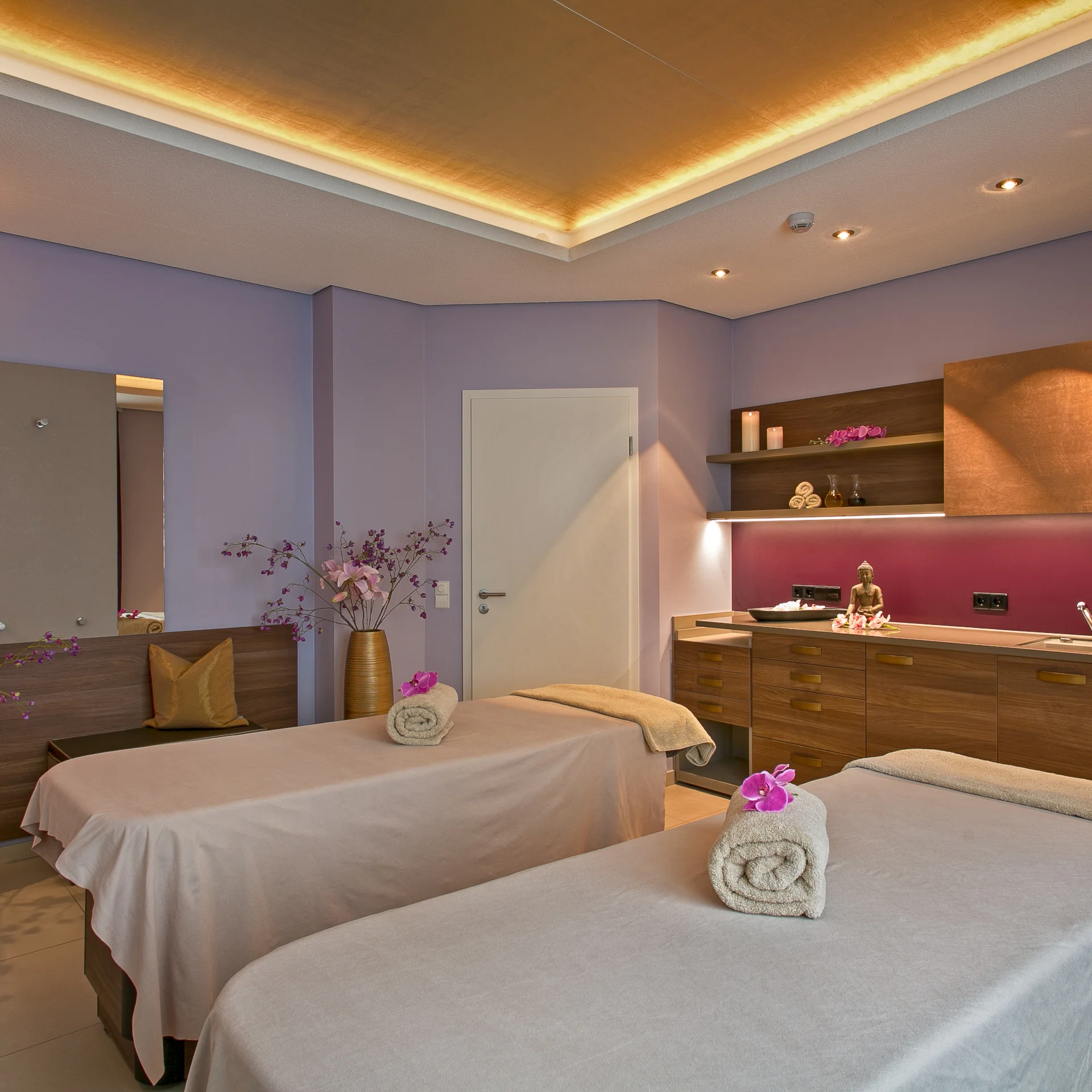 Massagezimmer mit zwei Liegen, warm beleuchtet und dekoriert mit Blumen