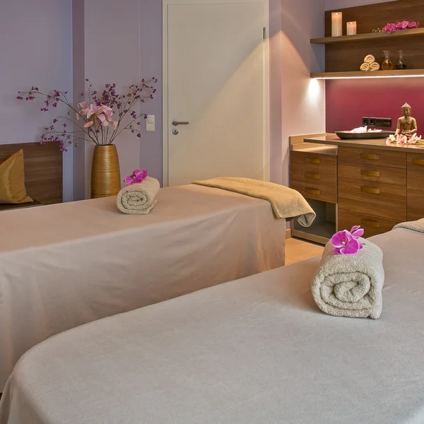 Massagezimmer mit zwei Liegen, warm beleuchtet und dekoriert mit Blumen