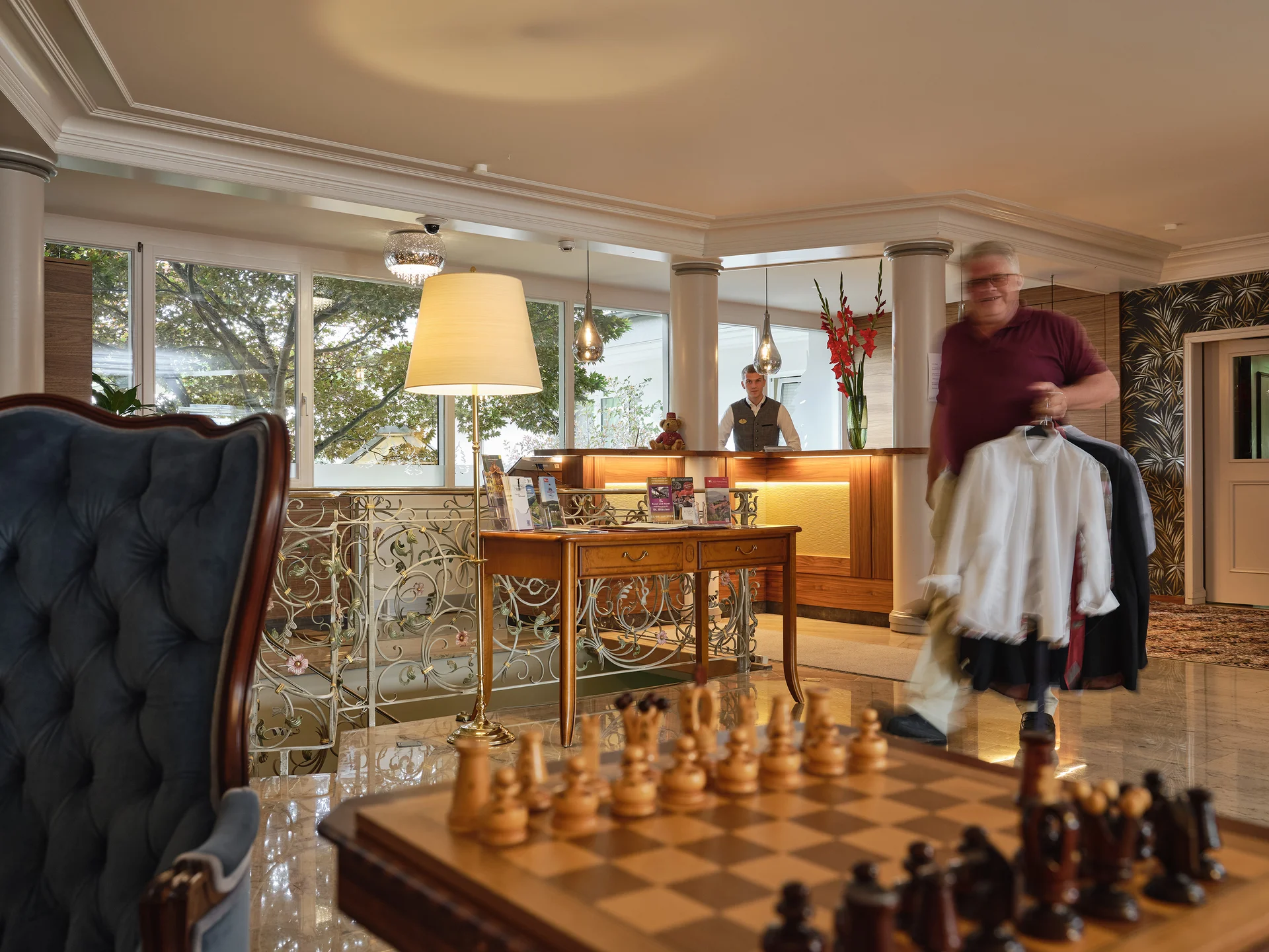 Hotelrezeption mit Warmlicht, Rezeptionist und älterem Mann mit Kleidung