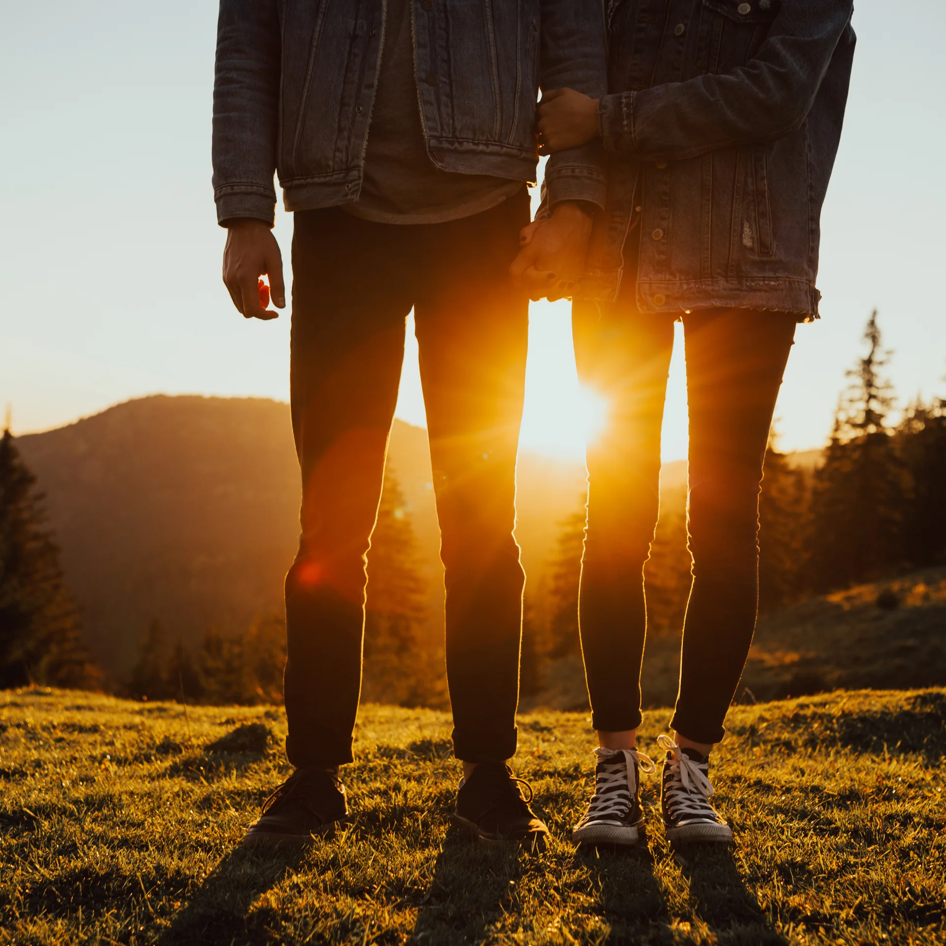 Zwei Personen halten Händchen mit Sonnenuntergang und Bergen im Hintergrund