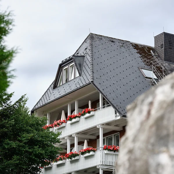 Wohnhaus mit grauem Schieferdach und Balkonen mit roten Blumen