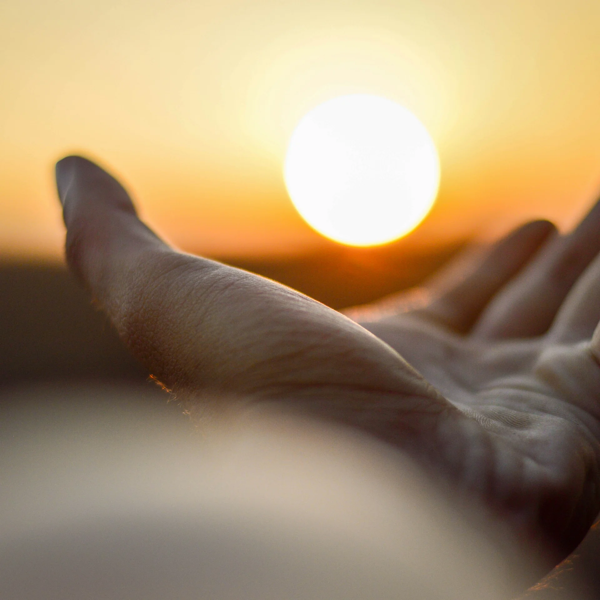 Hand, die bei Sonnenuntergang auf leuchtende Sonne zusteuert