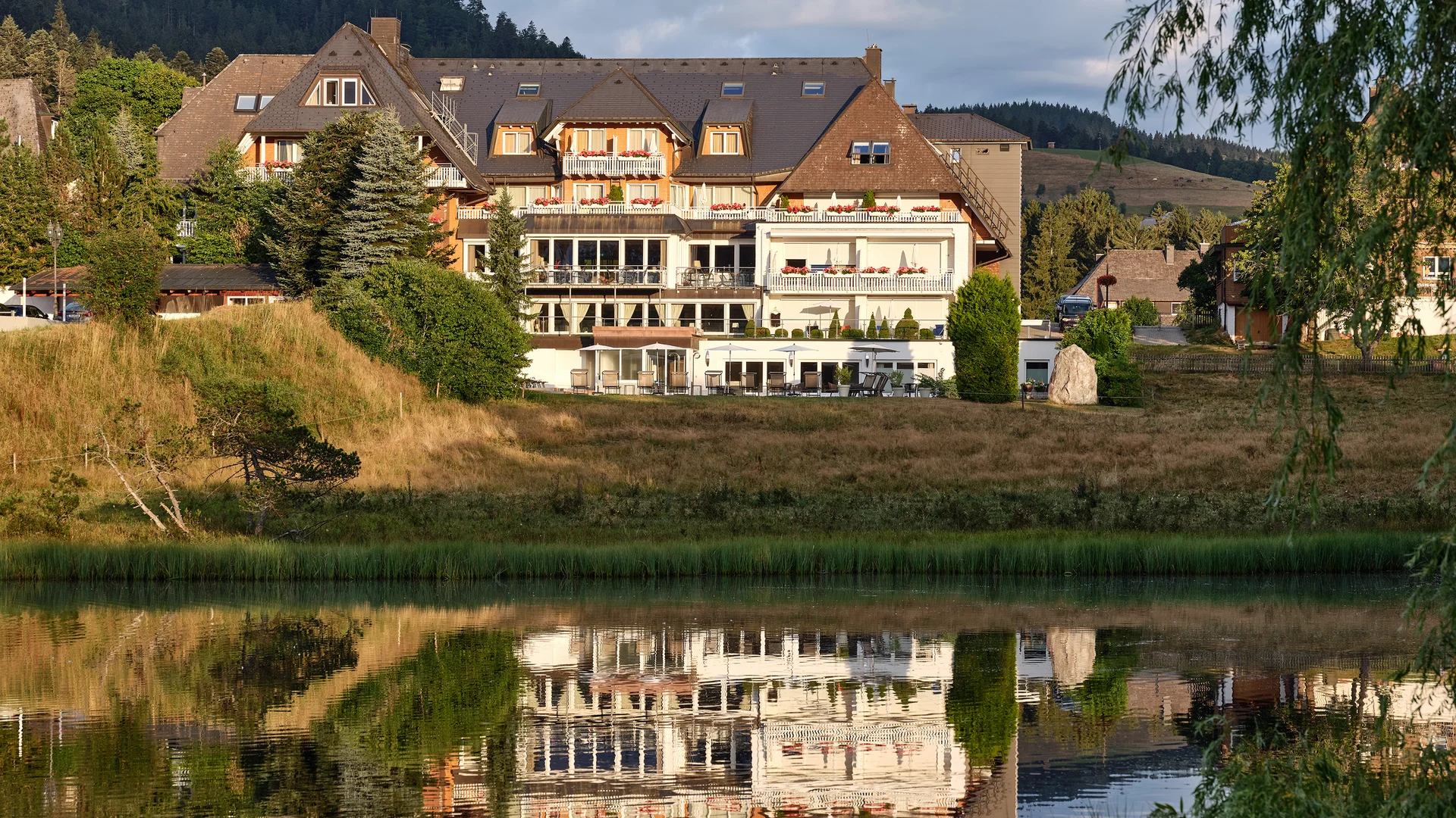 Hotelgebäude am See mit Spiegelung und Bergkulisse