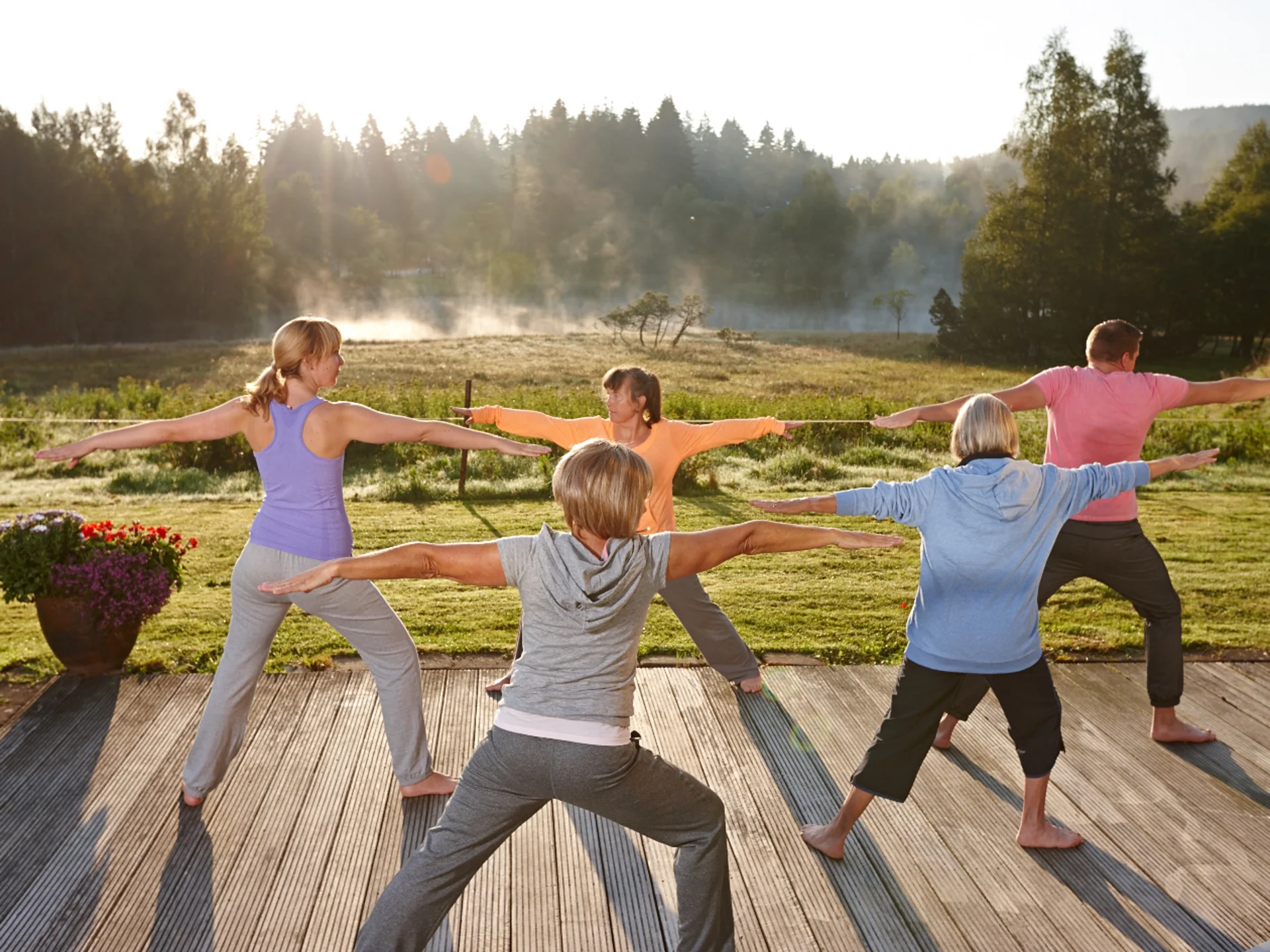 Gruppe praktiziert Yoga im Freien auf Holzdeck bei Sonnenaufgang
